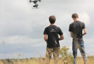 Twee dronepiloten op de rug bezien, en een drone in de lucht