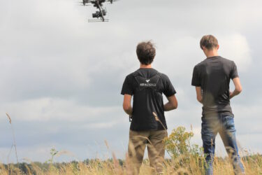 Twee dronepiloten op de rug bezien, en een drone in de lucht