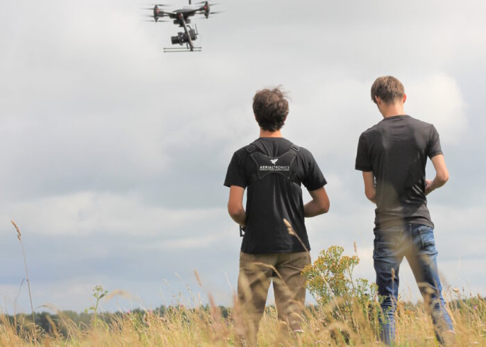 Twee dronepiloten op de rug bezien, en een drone in de lucht